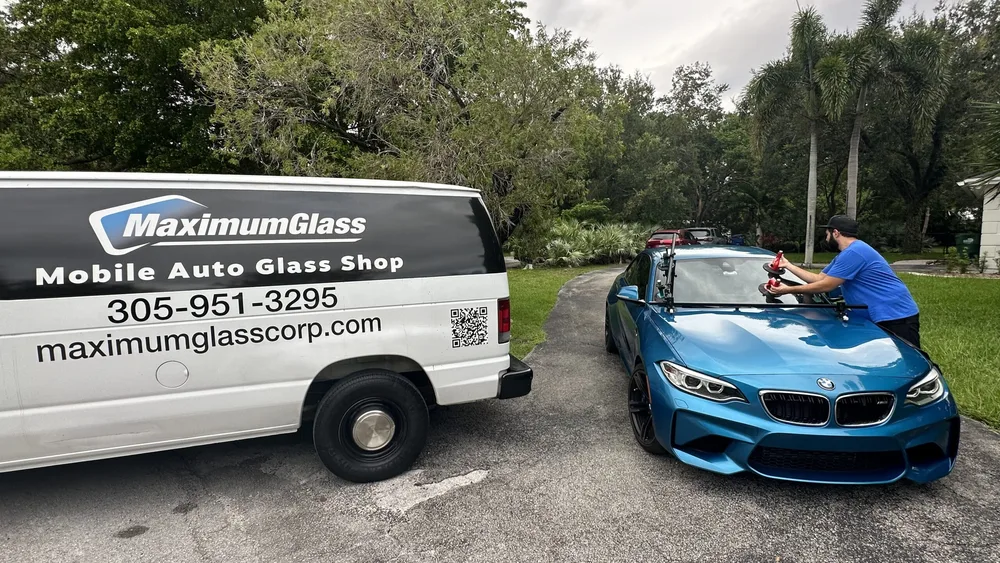 Technician setting a windshield on a blue BMW M2 convertible next to the Maximum Glass van