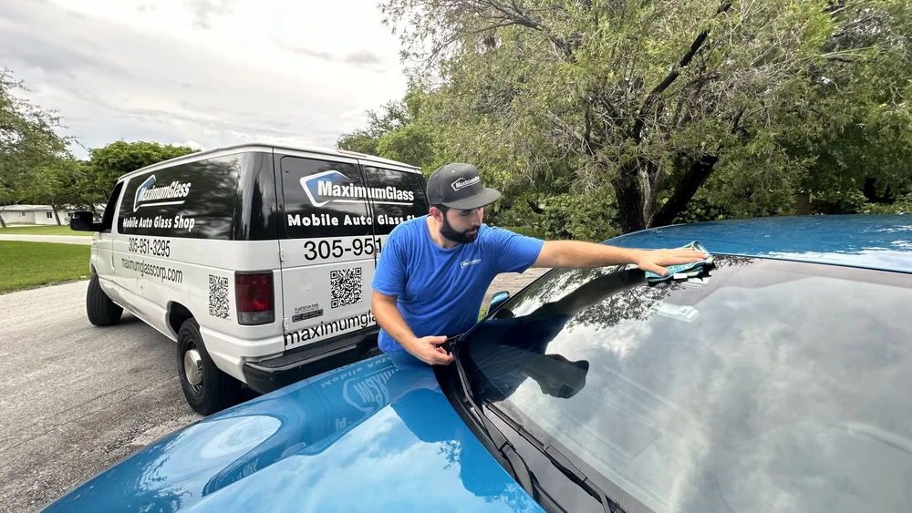 Technician wiping down the hood of a blue BMW beside the Maximum Glass service van