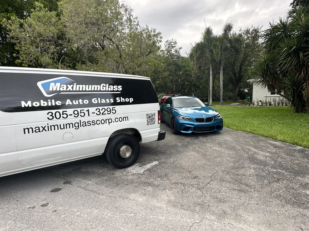 Maximum Glass service van parked beside a blue BMW M2 in a residential driveway