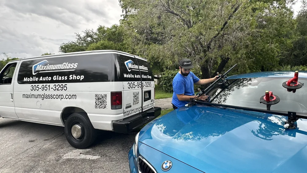 Technician working at the cowl of a blue BMW with the Maximum Glass van behind