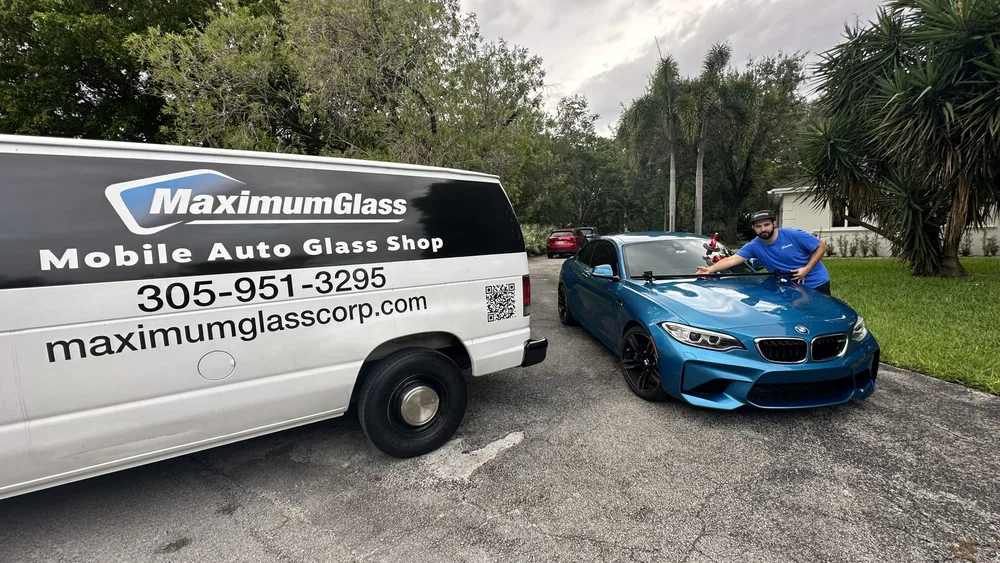 Maximum Glass van and technician working on a customer's BMW in a driveway under palm trees